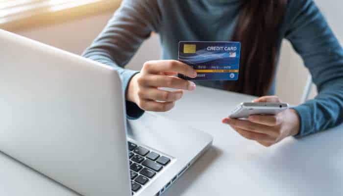 How to choose a cash back credit card that fits your spendin 1 | tycoonstory media Person using a laptop to make an online payment, holding a credit card and a smartphone over the keyboard.