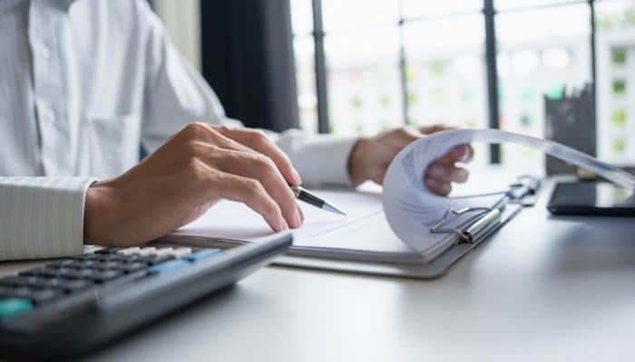 How to judge article quality-30kb | tycoonstory media Person's hands review documents at a bright office desk, with a calculator, pen, and papers nearby.