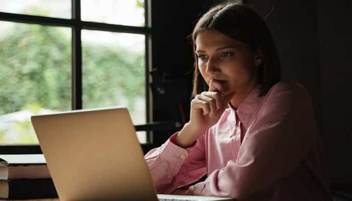 Why keywords alone are no longer enough | tycoonstory media Woman in a pink shirt rests her chin on her hand while looking at a laptop screen by a window, appearing thoughtful or focused.