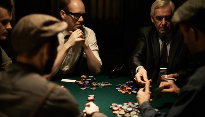 Online casino platforms 3 | tycoonstory media Group of men around a green poker table, piles of colorful chips, one player showing cards while others watch.