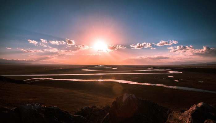 Real-money online casino games 3 | tycoonstory media Sunset over a winding river valley with reflective water, a dark rocky foreground, and scattered clouds in a bright sky.