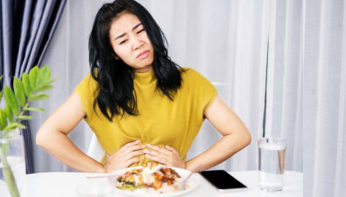 Should you eat when you have diarrhea | tycoonstory media Woman experiencing stomach discomfort while eating, related to how to stop diarrhea in adults fast.