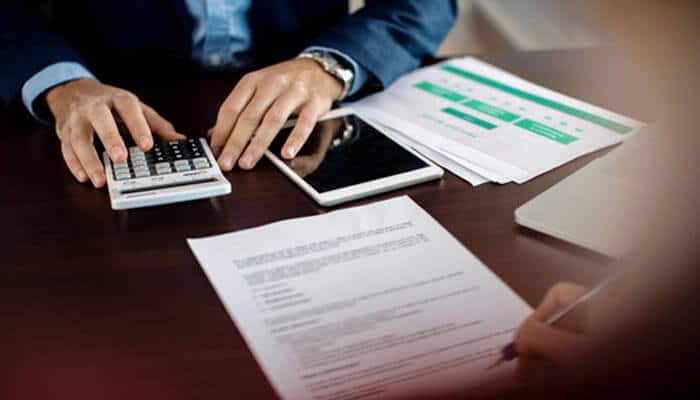 Review overhead regularly | tycoonstory media Business banking fees review showing a professional analyzing financial documents, payments, and account costs for better business management.