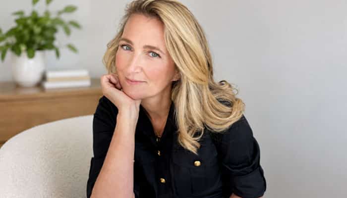 From essay to bestseller | tycoonstory media Woman with blonde hair sits in a chair, chin resting on her hand, smiling softly.