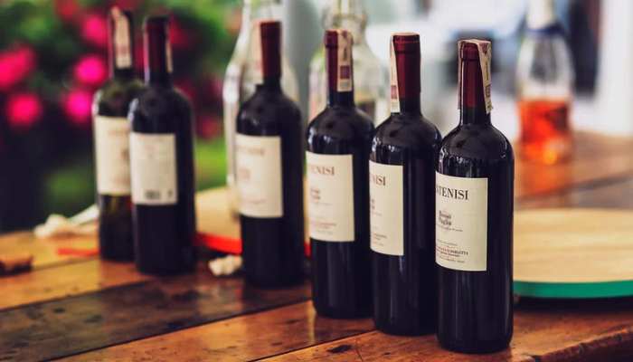 Why french wine is more than a drink 2 | tycoonstory media Five wine bottles lined up on a wooden table with a blurred café or tasting-room background.
