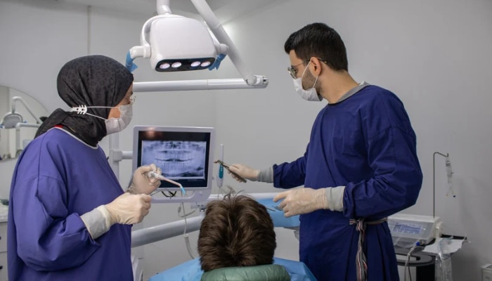 7 overlooked operational habits that keep dental practices profitable 1 | tycoonstory media Two dental professionals in scrubs and masks treat a patient, viewing a dental x-ray on a monitor during a procedure.