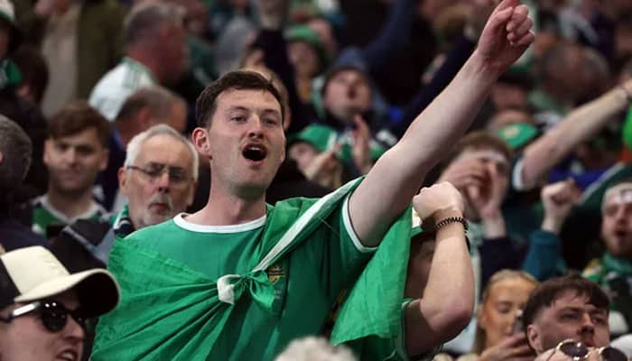 The green and white army and fan culture | tycoonstory media Supporter in a green shirt raises his fist and cheers at a crowded sports event