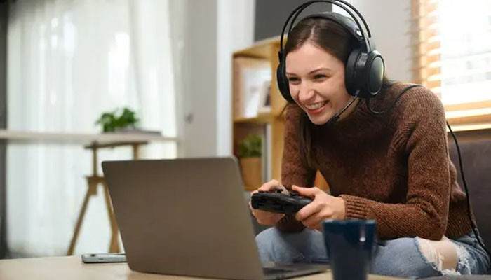 Can you play xbox games you already own - tycoonstory | tycoonstory media Woman wearing a gaming headset and holding a controller while enjoying xbox cloud gaming on a laptop from her living room.