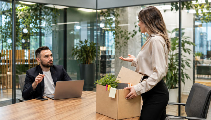 Give employees and customers clear information | tycoonstory media Woman stands with a moving box of items, handing it to a man seated at a conference table in a modern glass-walled office.