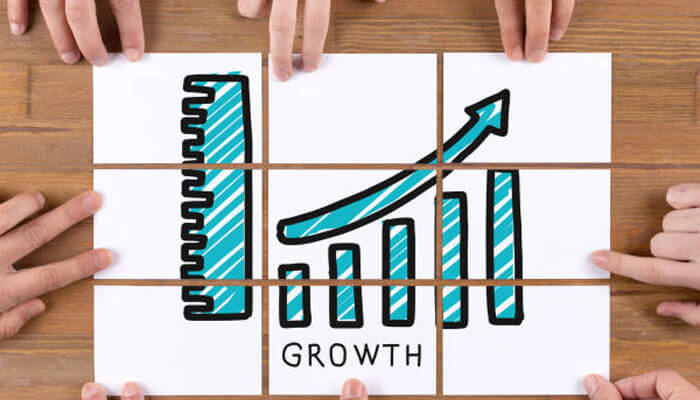 Give growth a small operating scorecard | tycoonstory media Hands assemble white tiles forming a growth chart with rising bars and a blue upward arrow labeled growth on a wooden table.