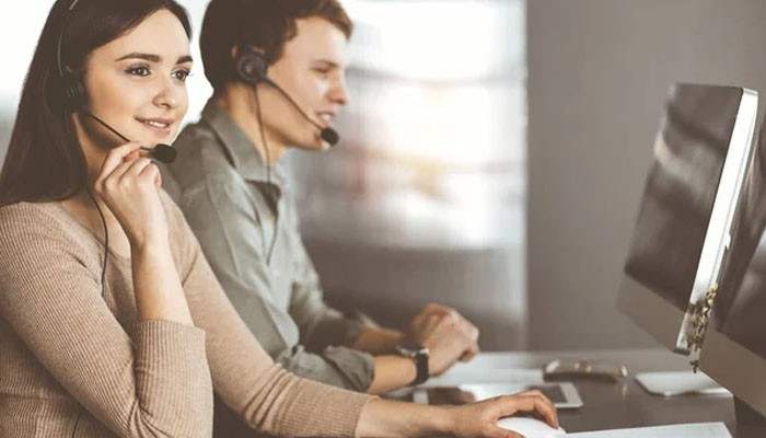 Improving customer experience and service responsiveness | tycoonstory media Two customer service agents wearing headsets work at computer desks in a bright office, assisting callers or clients.