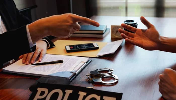 High-value investigations and law-enforcement work | tycoonstory media Police interview scene: hands gesturing across a desk with a notebook, pen, smartphone, and handcuffs near a police badge on the table.