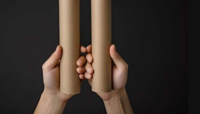 Manufacturing and production | tycoonstory media Two hands gripping vertical cardboard tubes against a dark background.