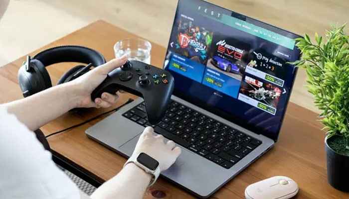 How microsoft xbox is changing the gaming industry - tycoonstory | tycoonstory media Microsoft xbox gaming experience featuring a player holding an xbox wireless controller beside a laptop displaying digital games.