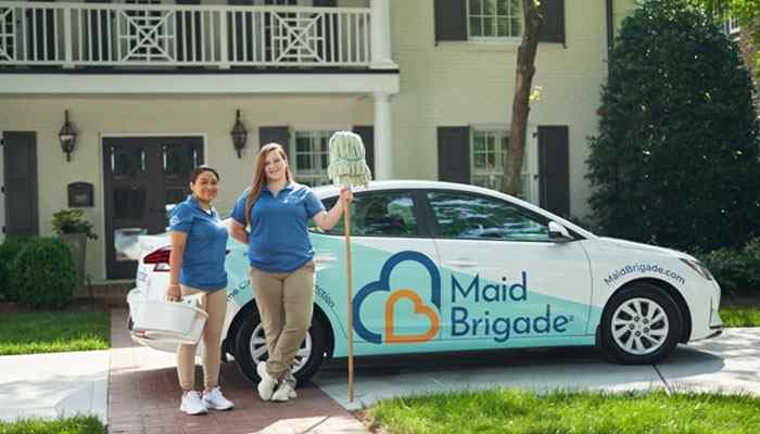Maid brigade (oakland and macomb counties) | tycoonstory media Two maid brigade cleaners pose beside a branded car with a teal and blue logo on a suburban driveway.