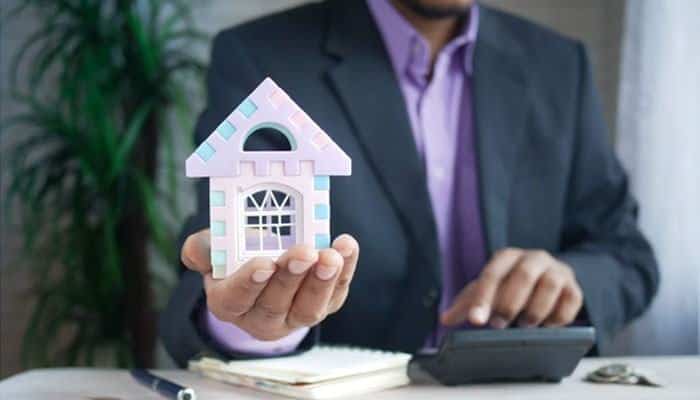 What a provider comparison looks like in practice | tycoonstory media Person in a suit presenting a small pastel house model at a desk.