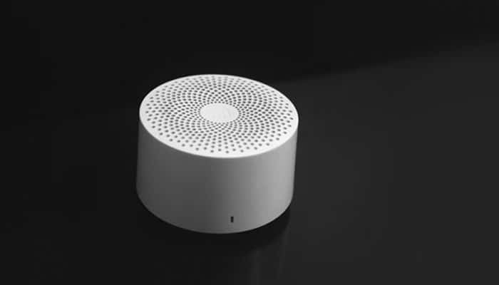 Innovative features transforming user experience | tycoonstory media White cylindrical portable speaker with a perforated top on a dark surface.