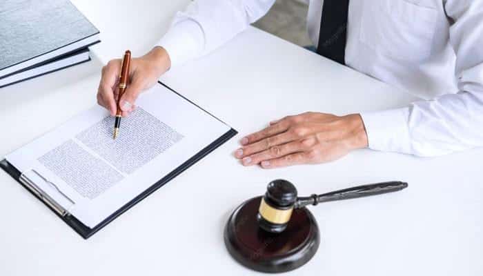 Davis injury lawyers, pllc | tycoonstory media Person in a white coat signs a document with a pen at a desk, with a gavel nearby indicating a legal setting.