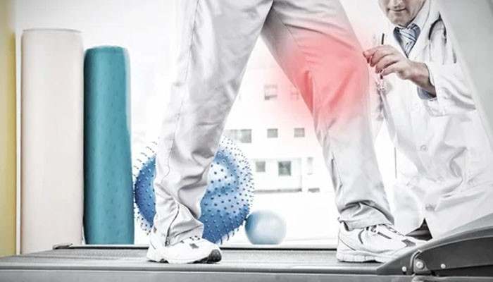 Modern lifestyles and the corporate body | tycoonstory media Therapist assists a patient walking on a treadmill; red glow on knee suggests pain or emphasis on treatment.