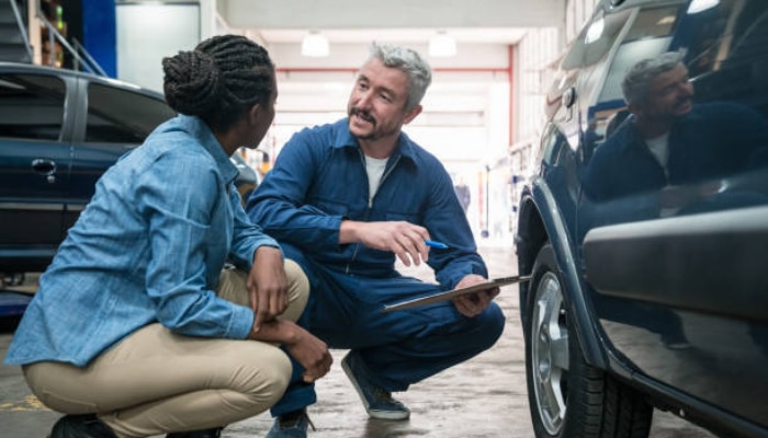 The attention to detail that keeps your car looking right 1 | tycoonstory media Mechanic explains car repair to a customer, pointing at a clipboard beside a blue suv in a workshop.