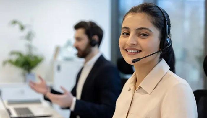 Reviews: 10 best ai virtual receptionists for customer service calls in 2026 | tycoonstory media Customer service representative with a headset smiles at the camera in a call center. This option keeps focus on the communicator and role in a busy office setting.